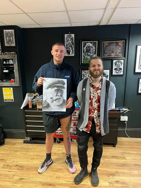 apprentice holding black and grey old man drawing, artist beside him