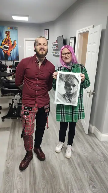 tattoo artist and client holding a black and grey portrait drawing