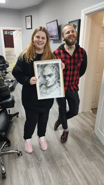 tattoo artist and client holding black and grey portrait drawing