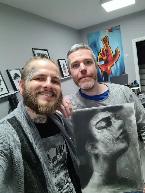 two men holding black and grey abstract face drawing