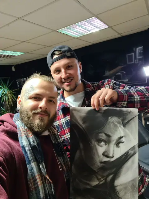 two men holding black and grey female portrait drawing