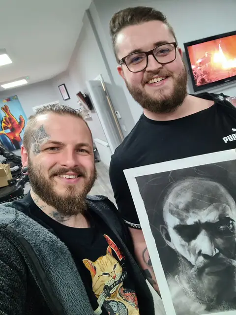 two men holding black and white print of bearded man's face