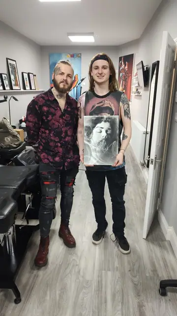 two men holding up artwork in a tattoo studio