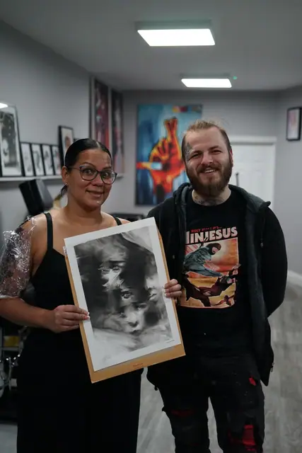 woman and man holding black and grey abstract tattoo design drawing