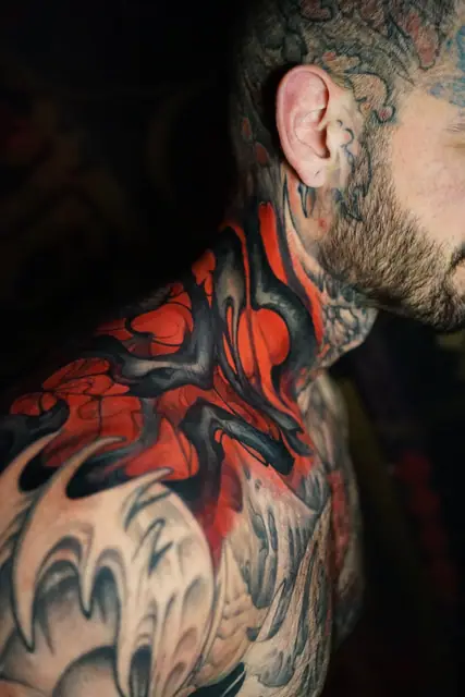 abstract red and black flowing biomech tattoo on neck and shoulder