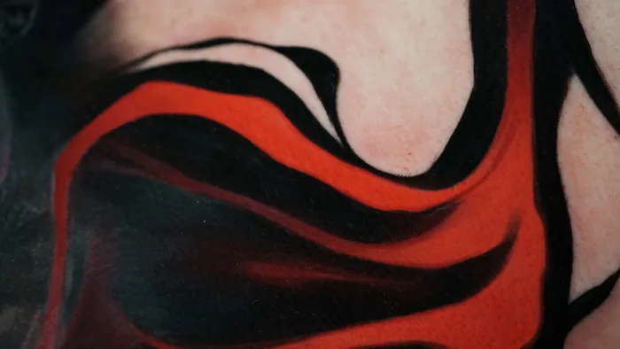 close-up detail of red and black abstract flowing tattoo on skin