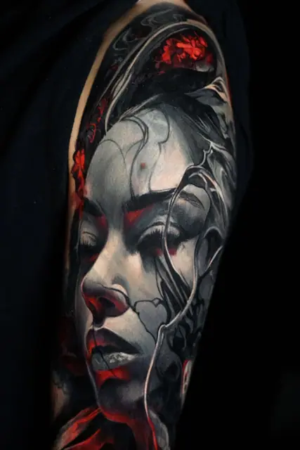 black and grey woman's face tattoo with red accents on upper arm