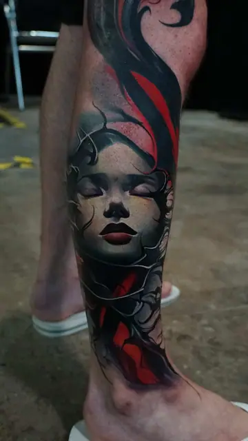 colour realism woman's face and abstract shapes tattoo on lower leg