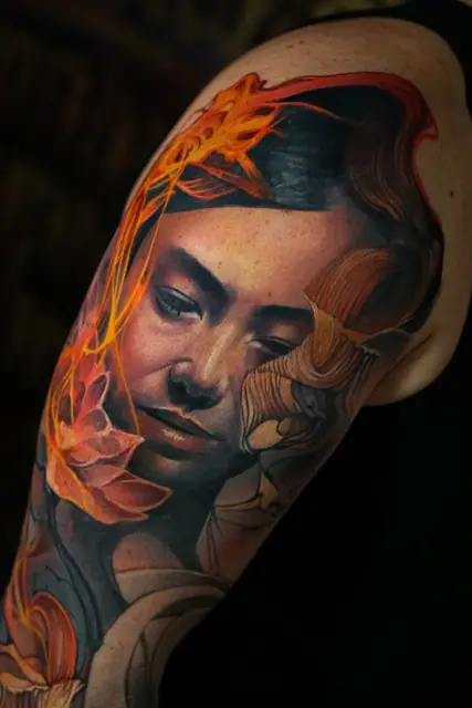 colour realism woman's face and flowers tattoo on upper arm