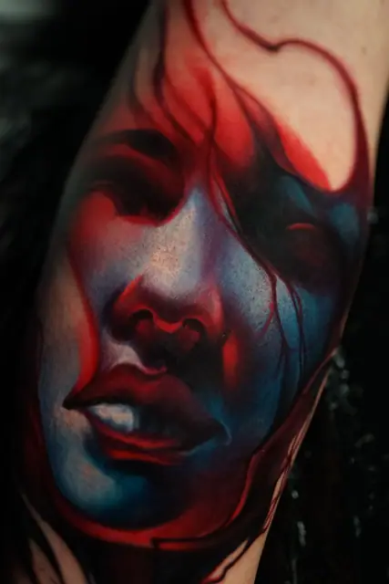 colour realism woman's face tattoo with red and blue tones on arm