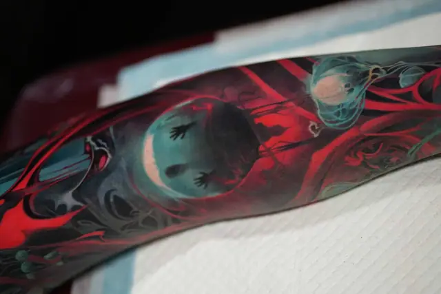 surreal red and teal celestial horror tattoo on forearm